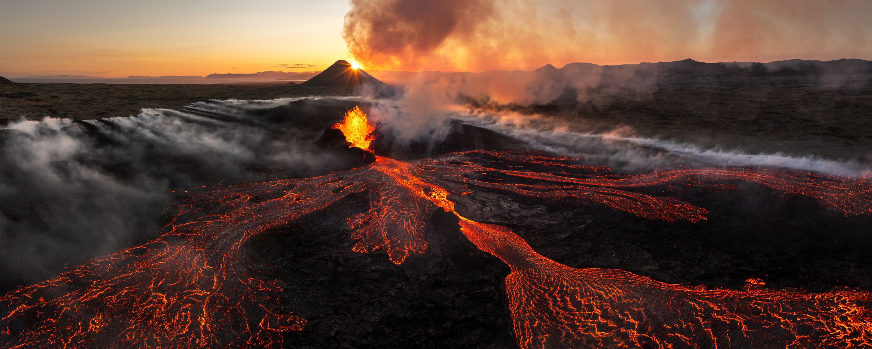 An aerial view of lava flowing in several directions from an erupting volcano.