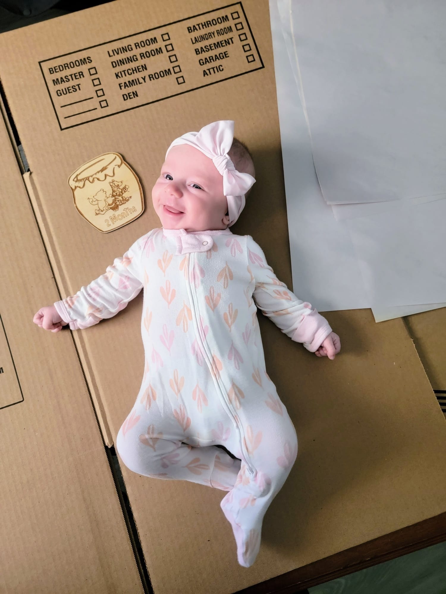A baby lies on a moving box next to a sign that says