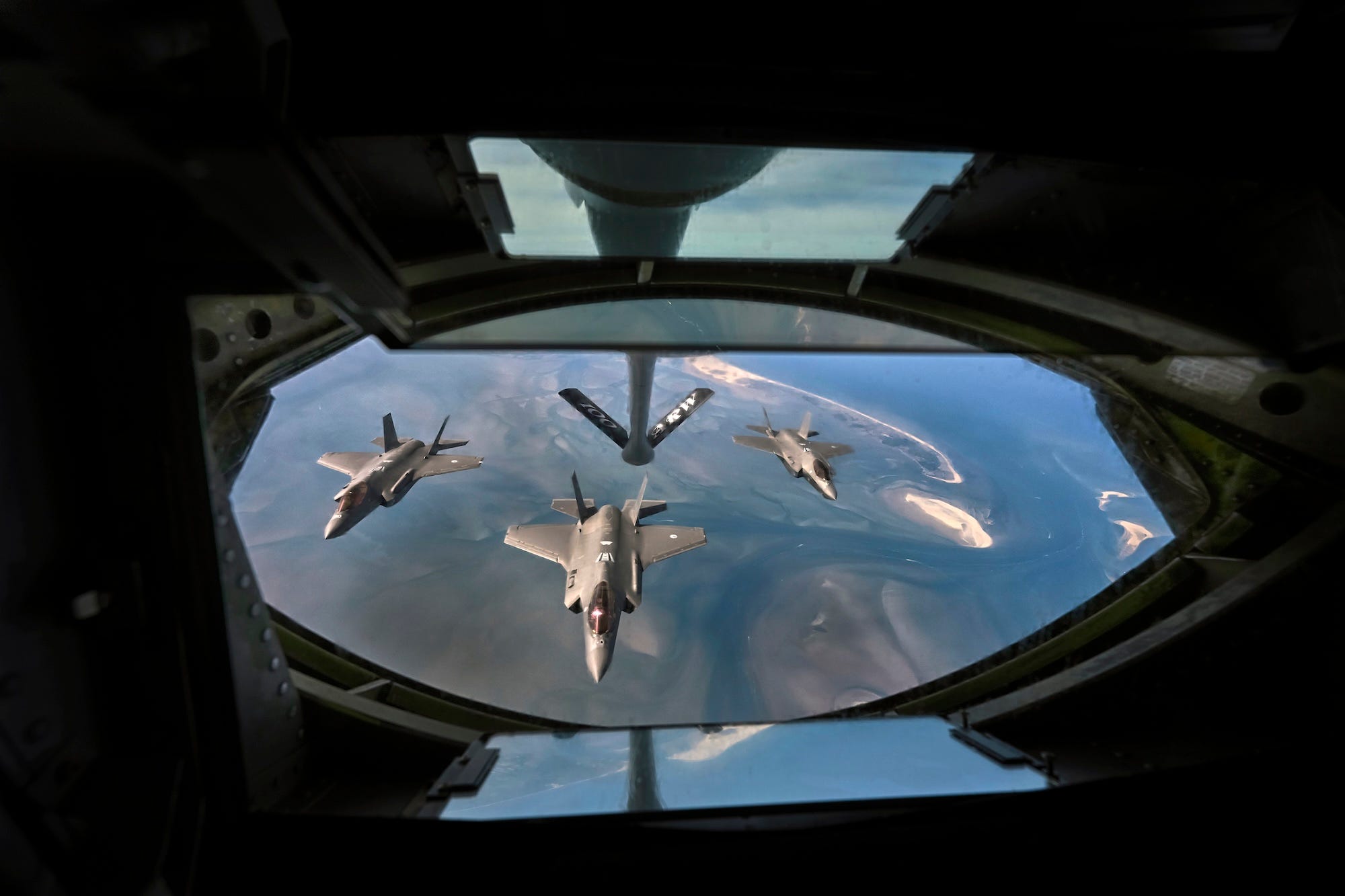Three grey fighter jets in the air pictured from inside another jet that is above them