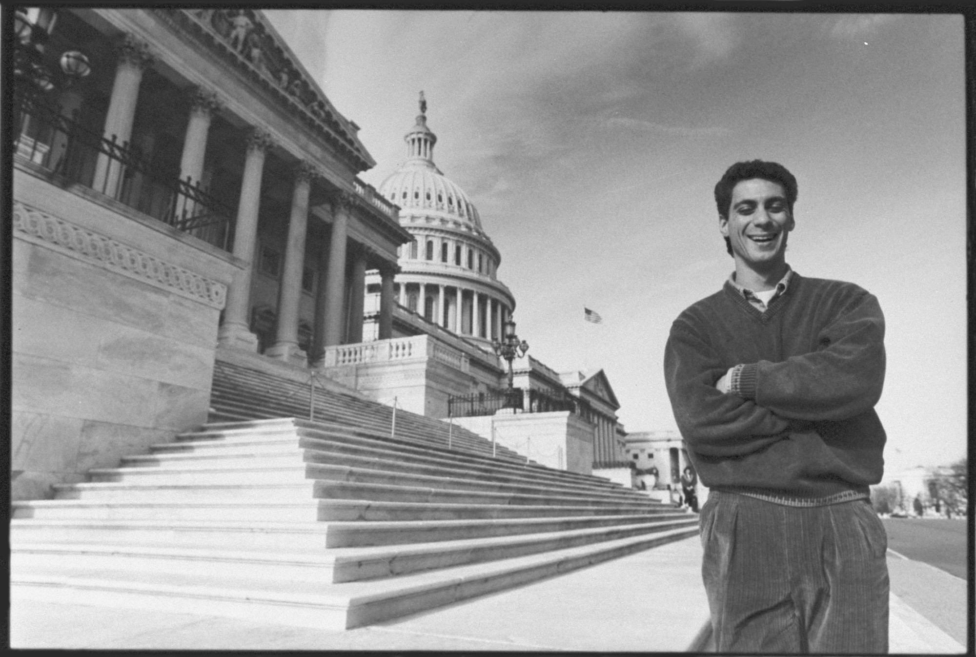A black & white image of a young Rahm Emanuel posing for a portrait in front of the U.S. Capitol.