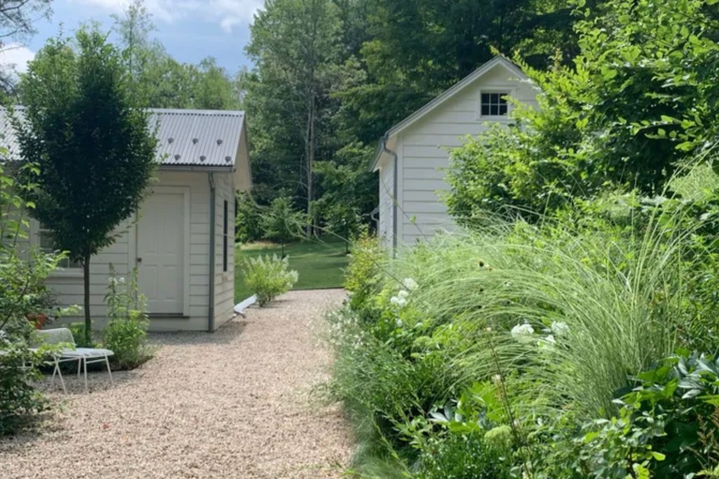 Gravel path leading to two white outbuildings surrounded by lush greenery.