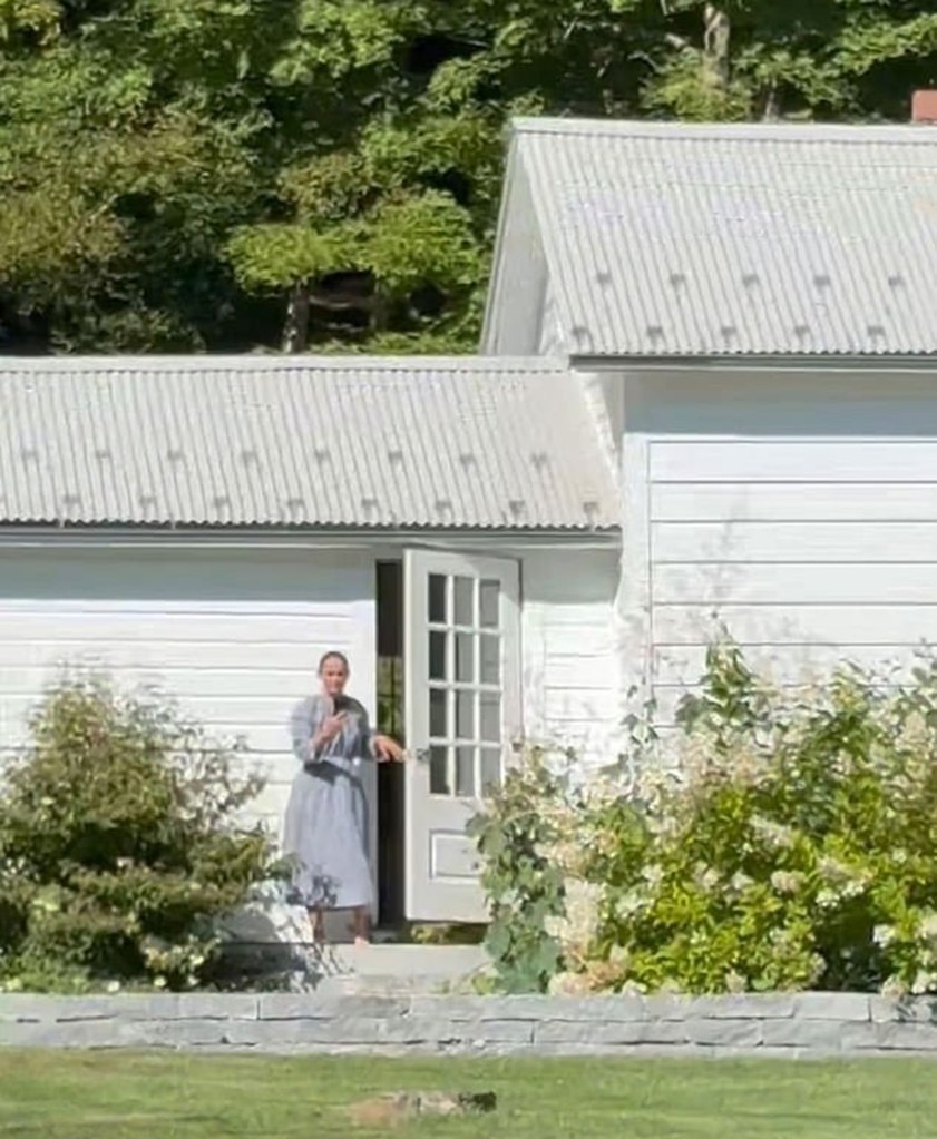 A woman in a blue dress stands in a doorway of a white house.