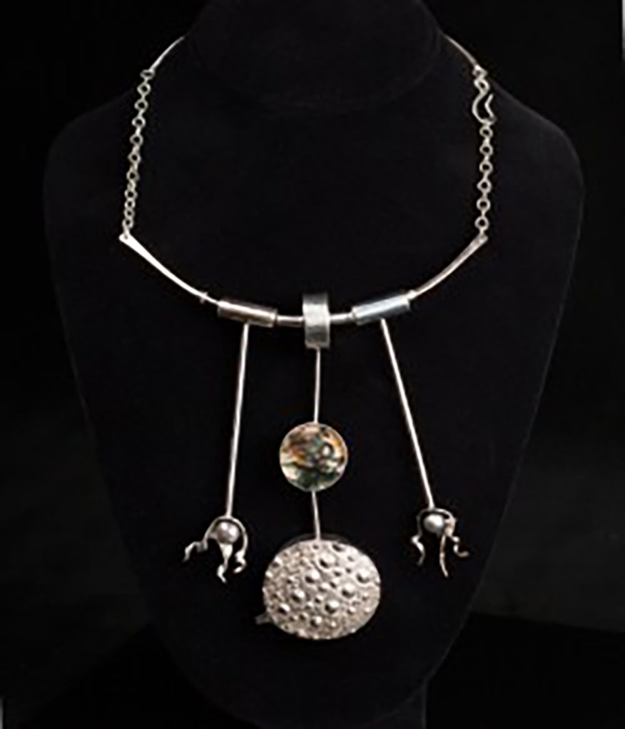 A silver necklace with three dangling pendants, two shaped like claws and one like a bumpy disc.