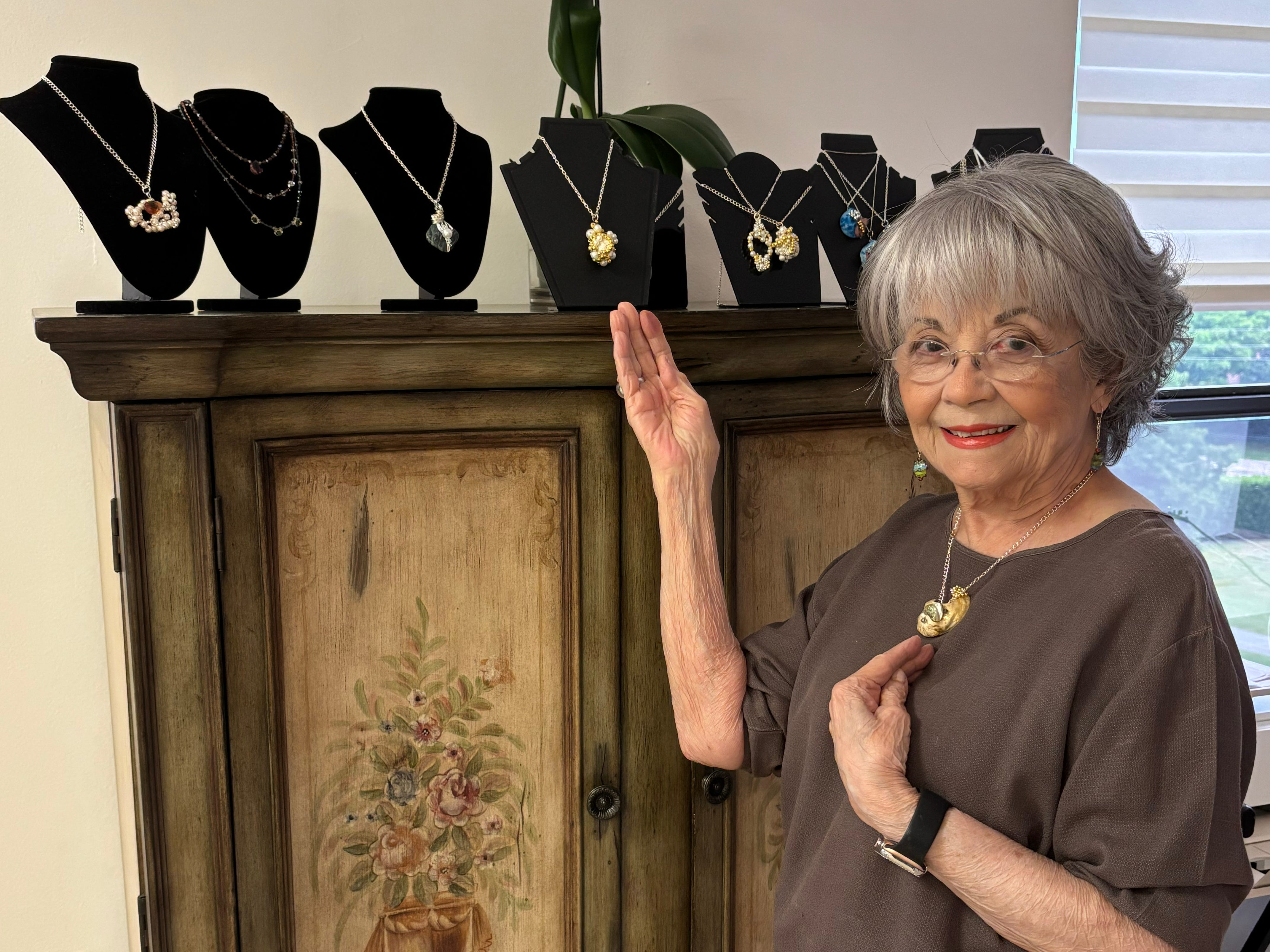 An older woman is pointing to some necklaces on a dresser