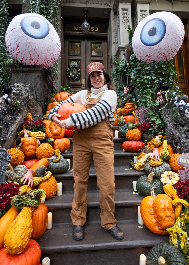 Hillary Simon holding a large pumpkin on her Halloween-themed stoop with various gourds and spooky decorations.