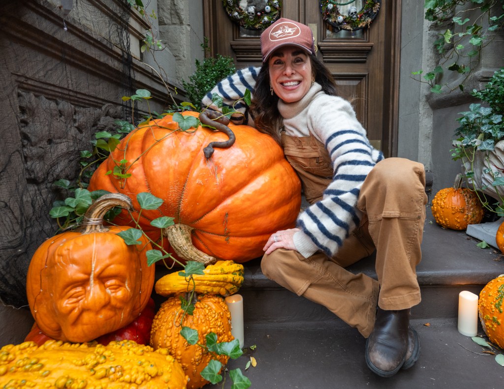 Hillary Simon poses on her Halloween-themed stoop adorned with pumpkins, gourds, and spooky decorations.
