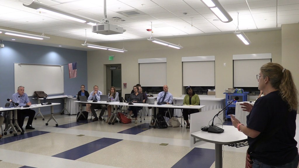 A woman speaking to a group of people sitting at tables.