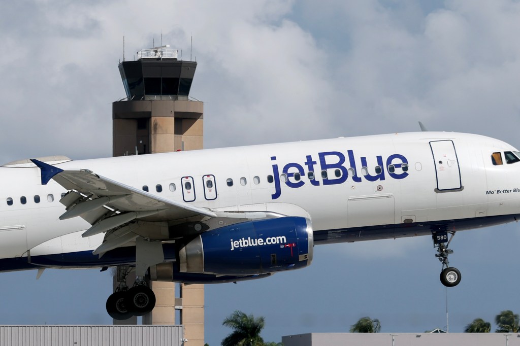 A JetBlue Airlines plane landing near an air traffic control tower.