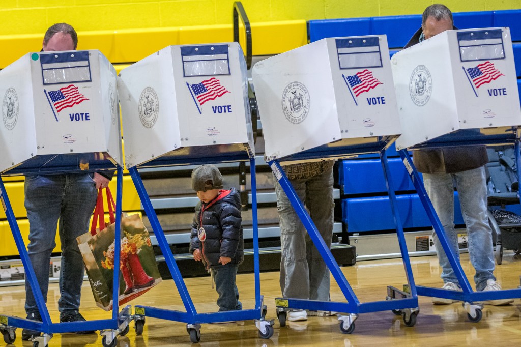 Voters casting ballots at voting booths, with a child in a winter coat standing between two booths.
