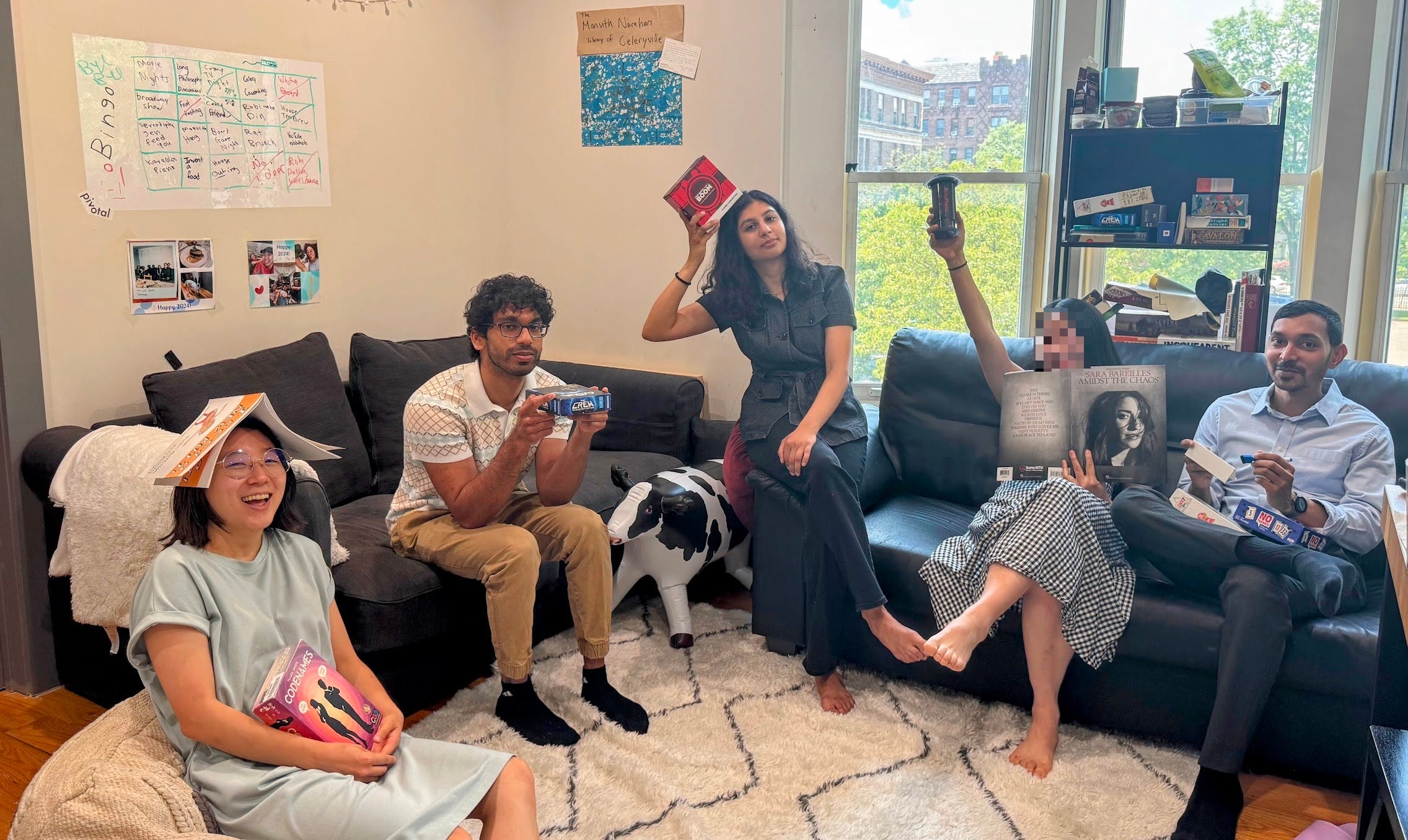 Jen Baik and friends, sitting on couches and holding up board games.