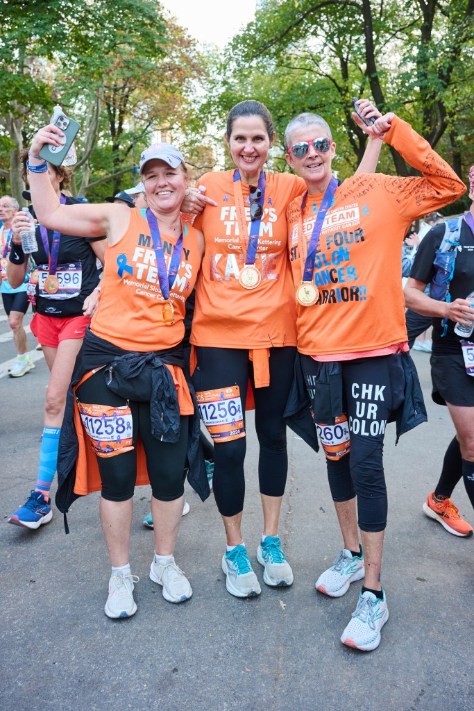 Three women, including Liz Healy, wearing orange shirts from Fred's Team posing after a marathon.