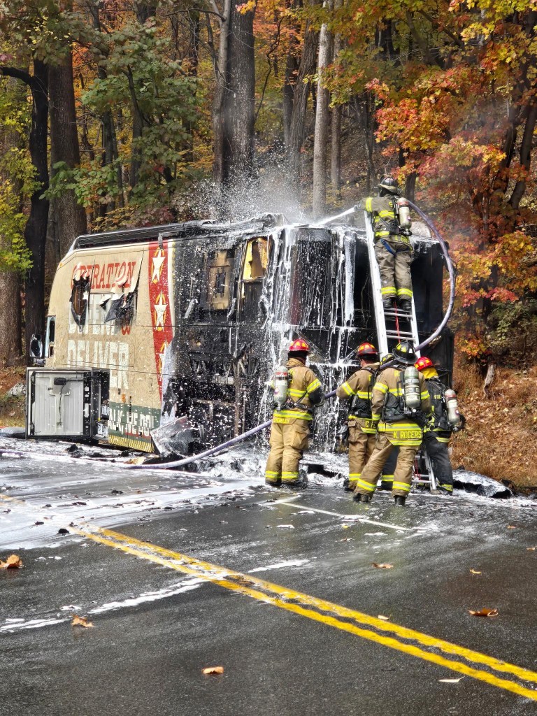 Firefighters extinguish the blaze of the bus on the side of the road.