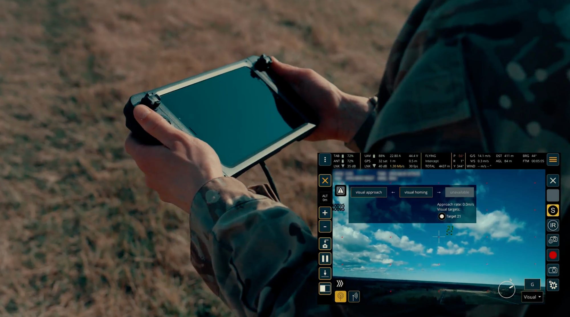 A pair of hands hold a controller with a screen with an inset of what the screen on the controller shows - a blue sky with a drone target identified