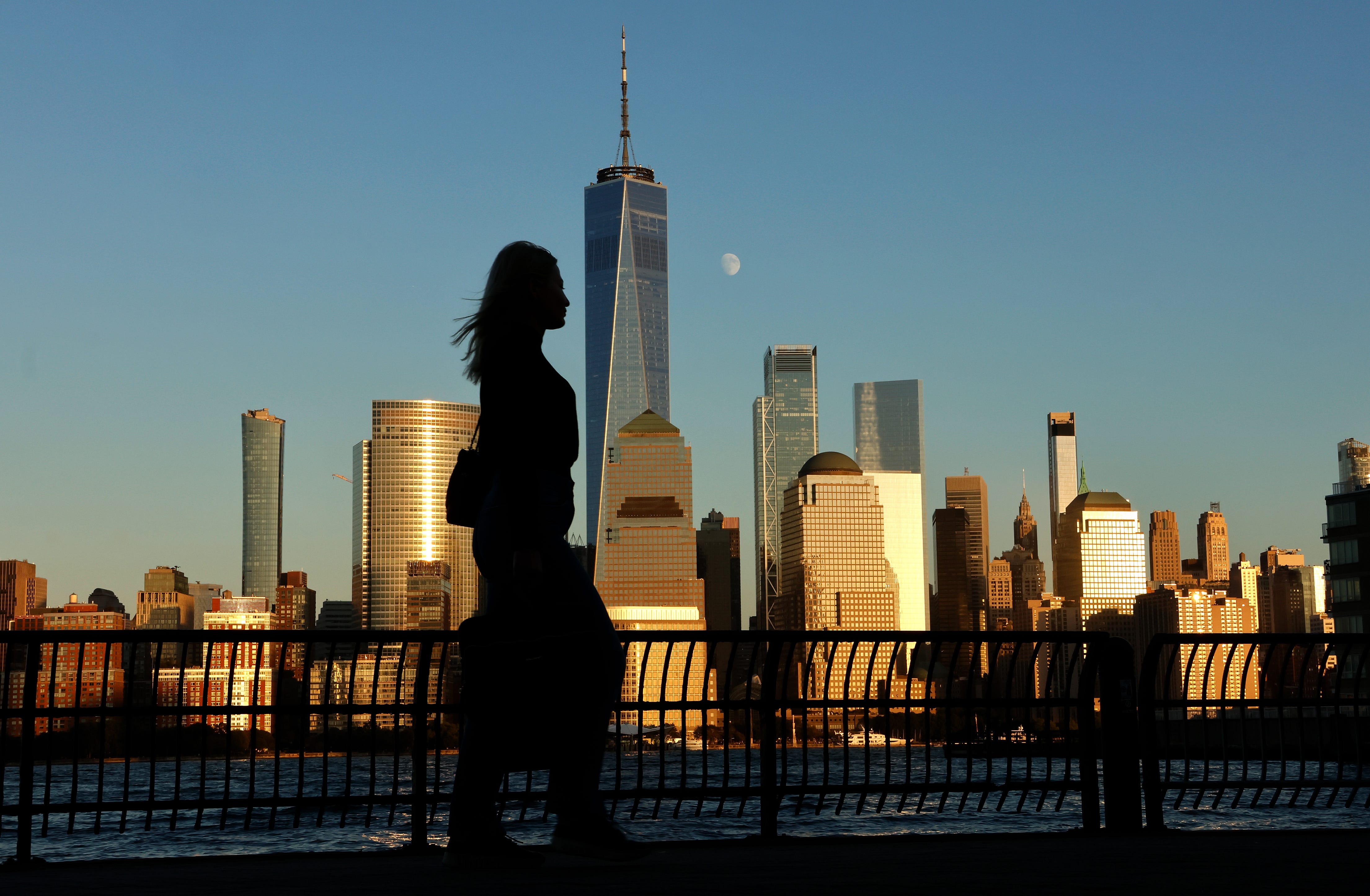 The moon rises behind the skyline of Lower Manhattan and One World Trade Center as the sun sets in New York City on October 3, 2025.