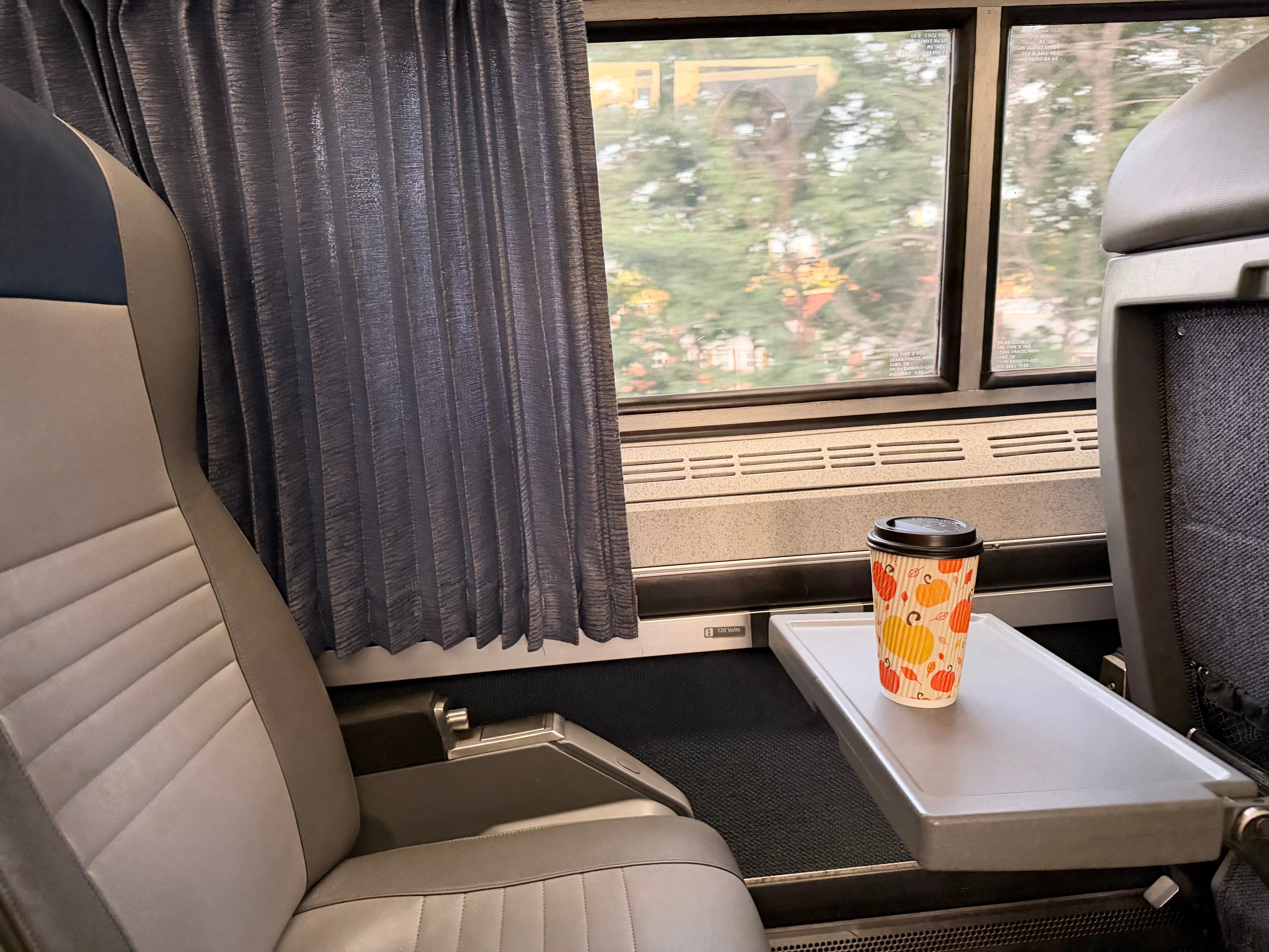 An Amtrak seat near the window, with a tray table pulled out in front of it.