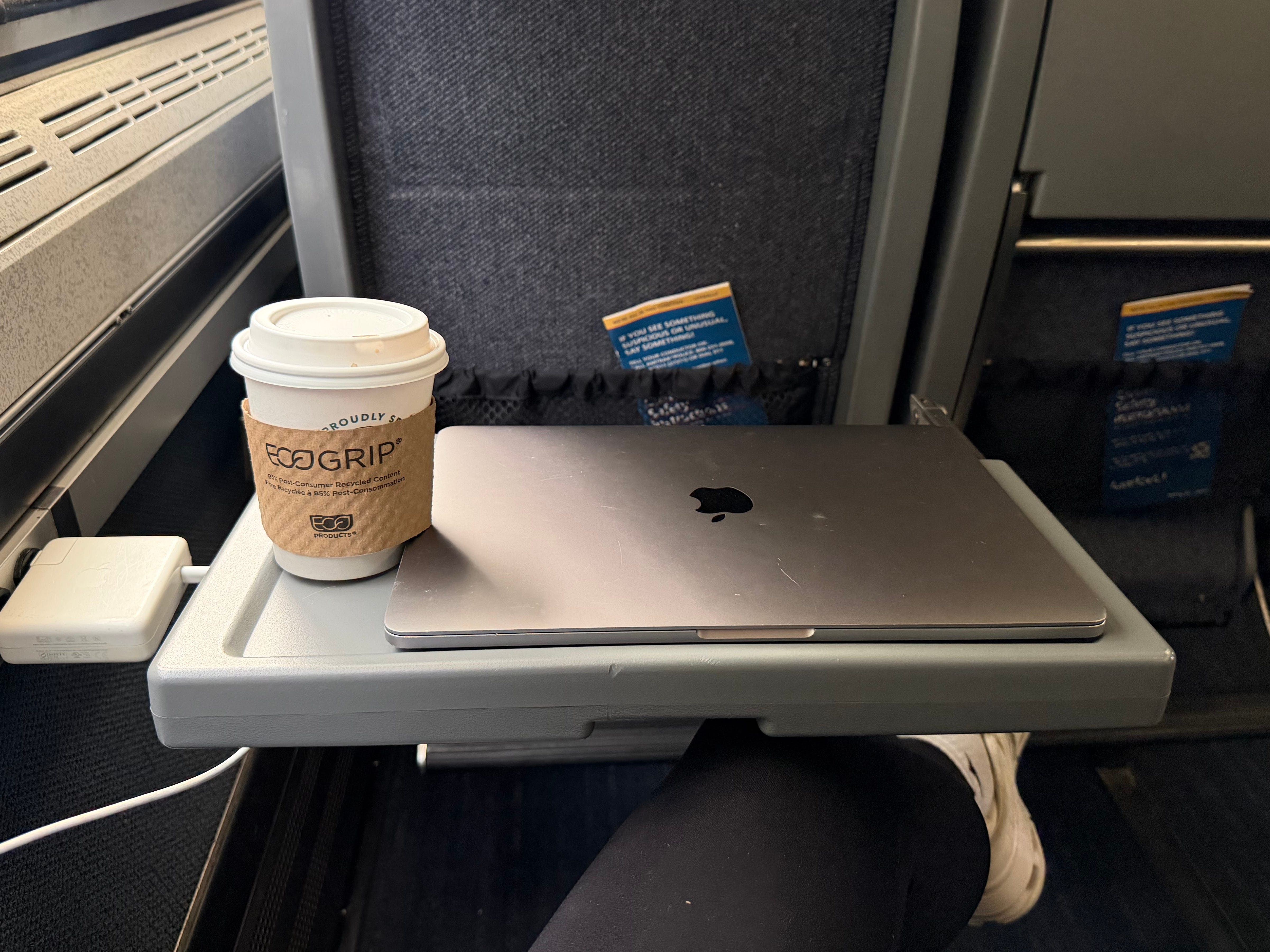 A tray table with a laptop and a cup of coffee on it.