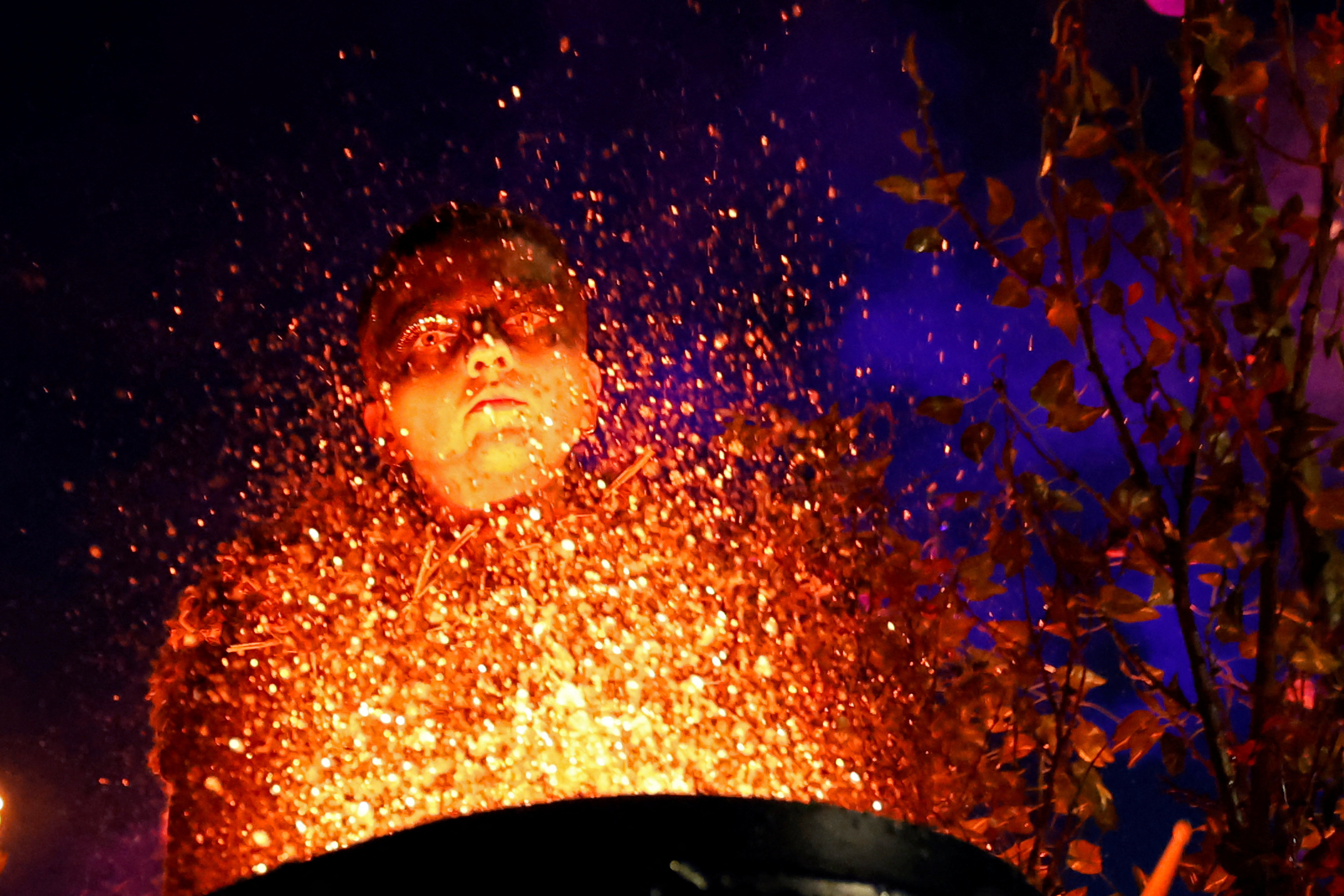 A performer, seen lit from below by an illuminated drum, with a splash of water rising from the drum, after it was struck.