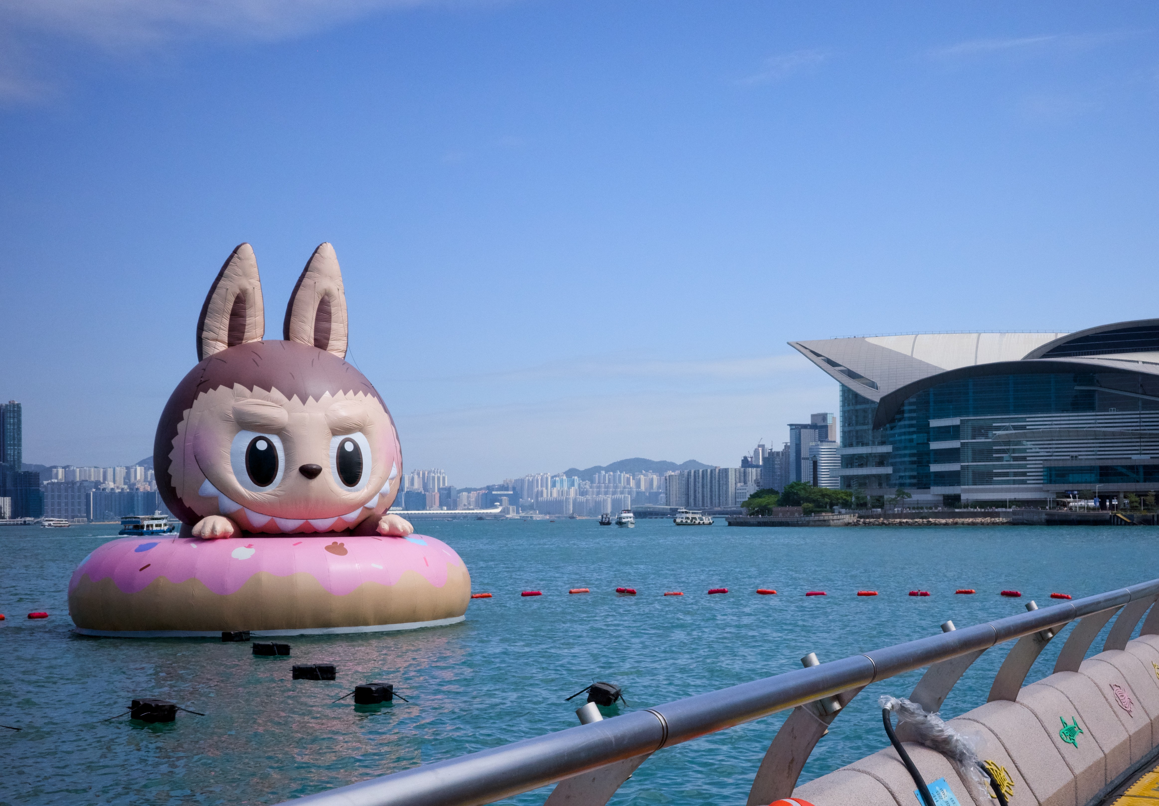 A giant inflatable sculpture of a Labubu floats in a harbor.