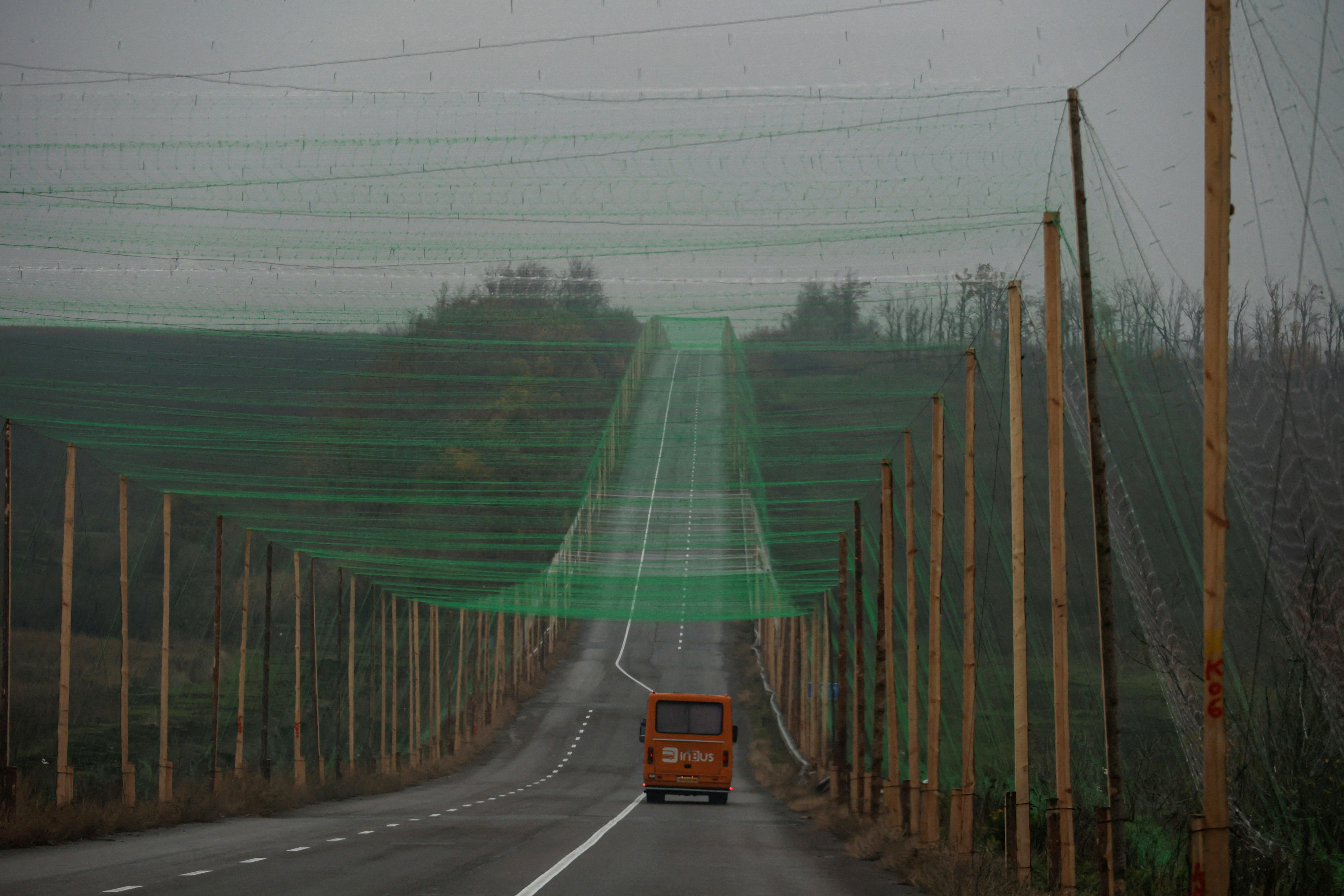 A car drives along a road covered with anti-drone netting, supported by tall poles on either side of the road.