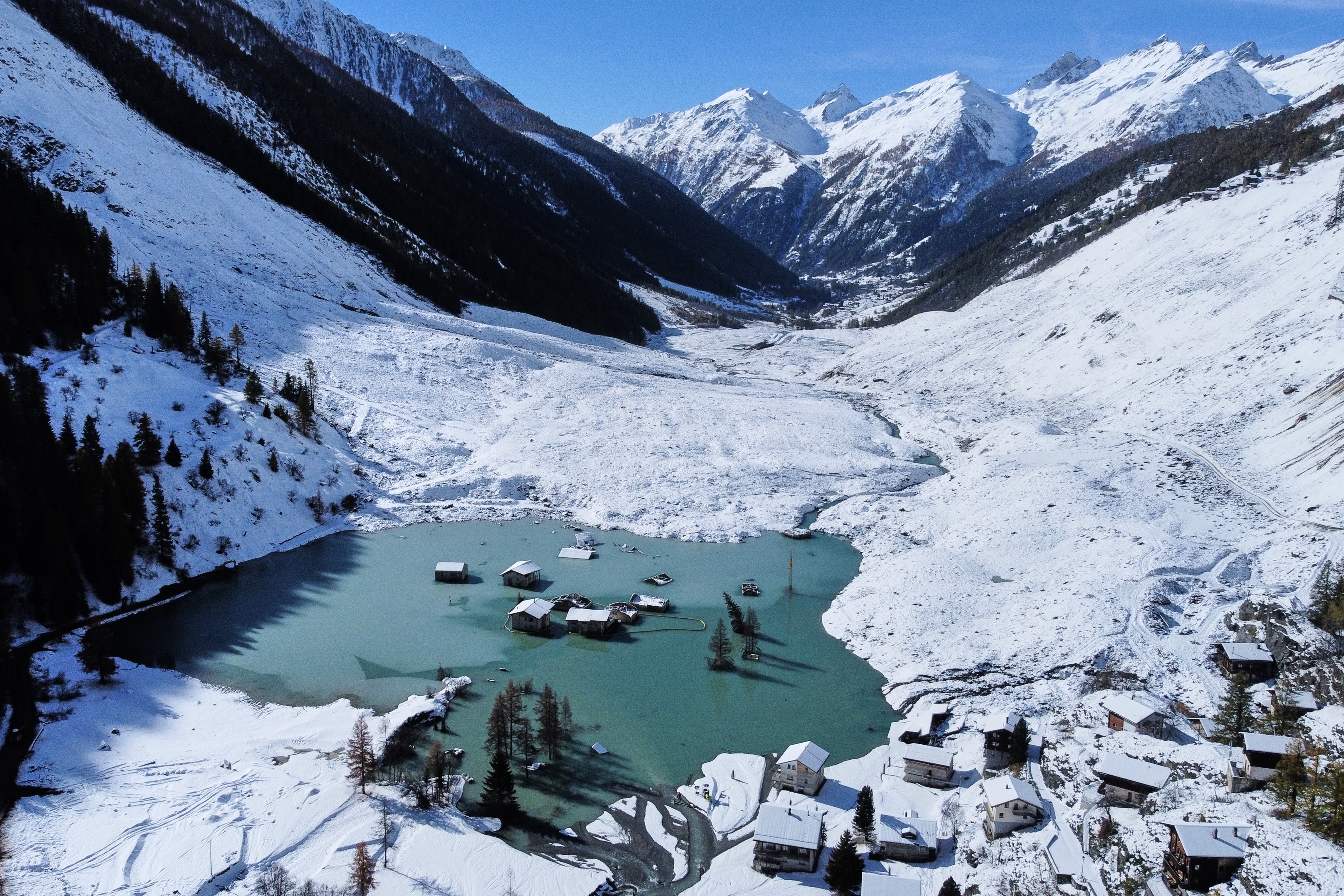 An aerial view of a partly-flooded village and debris from a landslide, mostly covered in recently-fallen snow