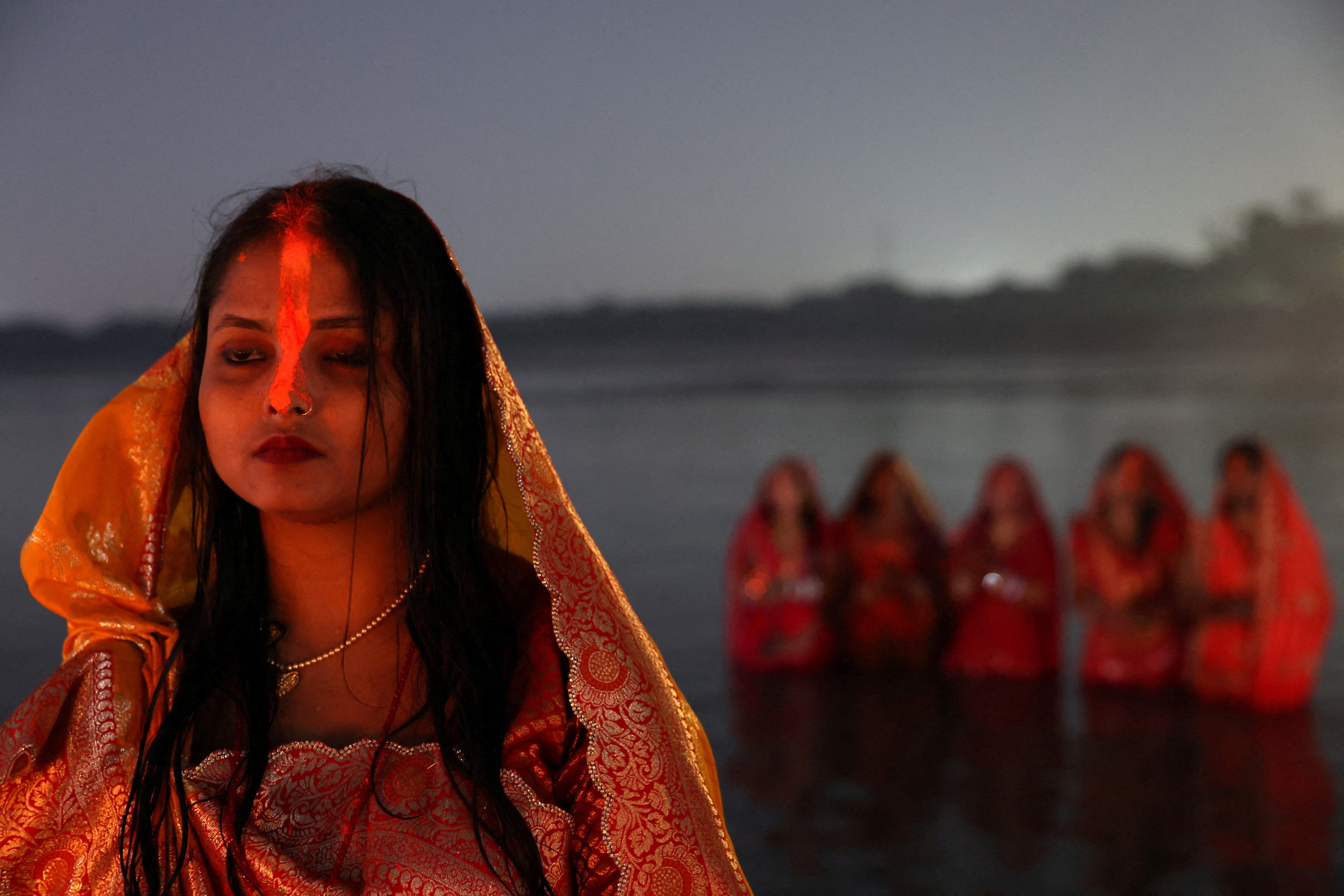 Groups of women stand in shallow river water to worship.