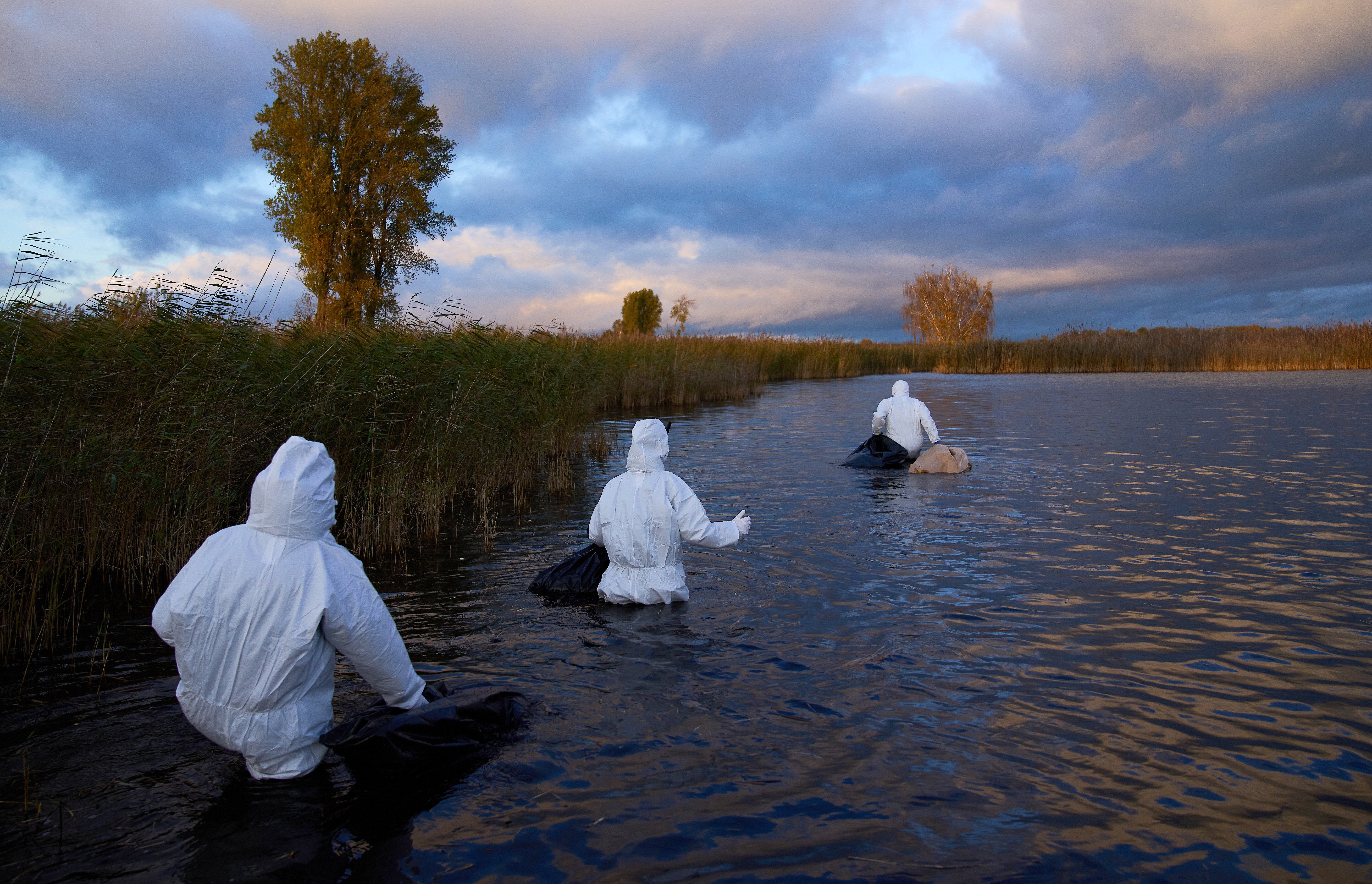 Several people in protective gear wade through waist-deep water