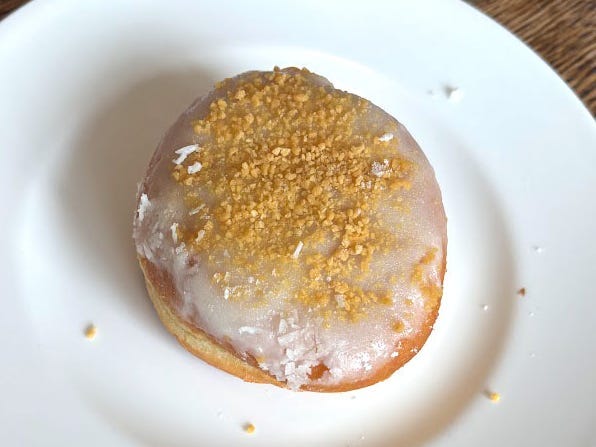 A doughnut topped with vanilla icing and apple crumbs on a white plate.
