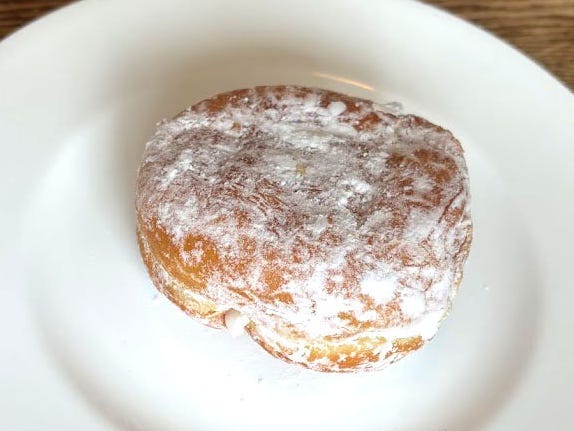 A doughnut with no hole topped with powdered sugar on a white plate.