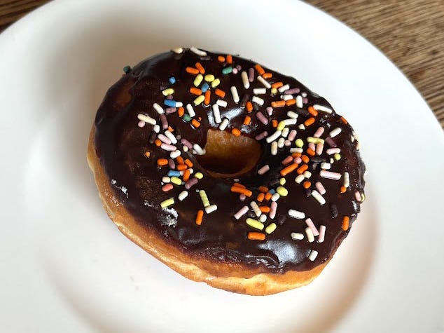 A doughnut with chocolate frosting and sprinkles on a white plate.