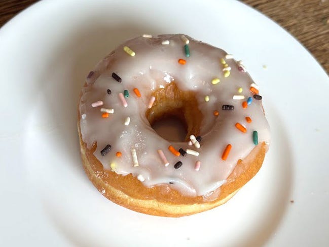 A doughnut with vanilla icing and sprinkles on a white plate.