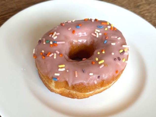 A doughnut topped with pink icing and sprinkles on a white plate.