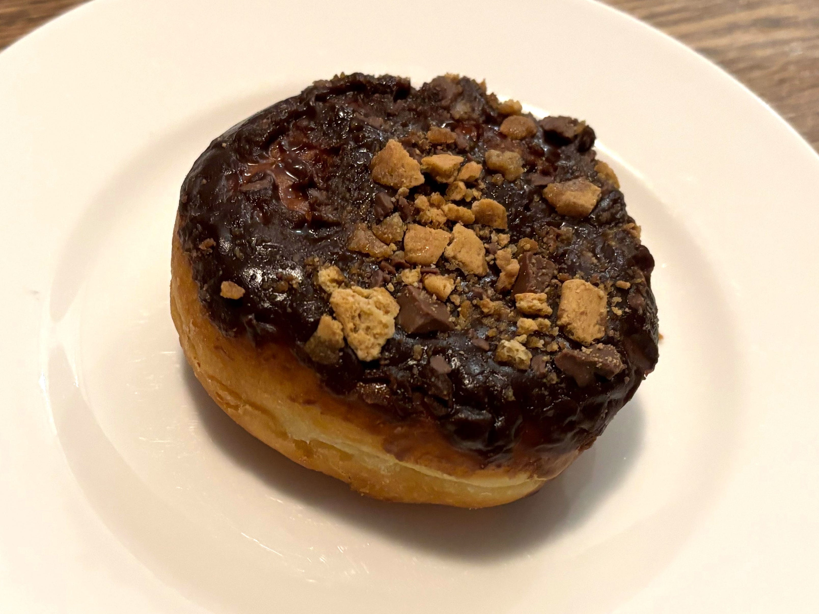 A doughnut with no hole topped with chocolate icing and graham-cracker pieces.