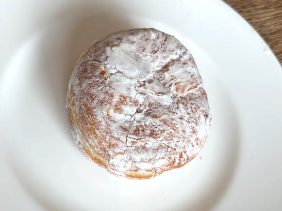 A doughnut with no hole covered in powdered sugar on a white plate.
