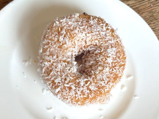 A doughnut topped with shredded coconut on a white plate.