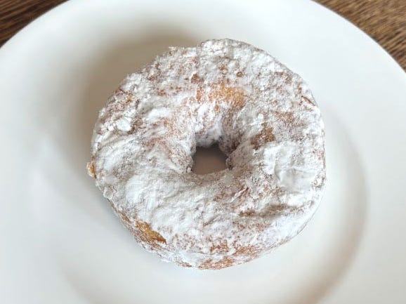 A doughnut topped with powdered sugar on a white plate.