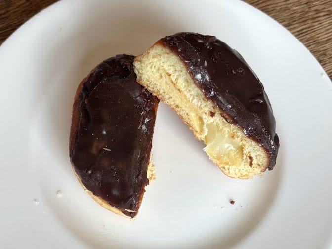 A doughnut with no hole, cut in half on a white plate. The doughnut is filled with cream and topped with chocolate icing.