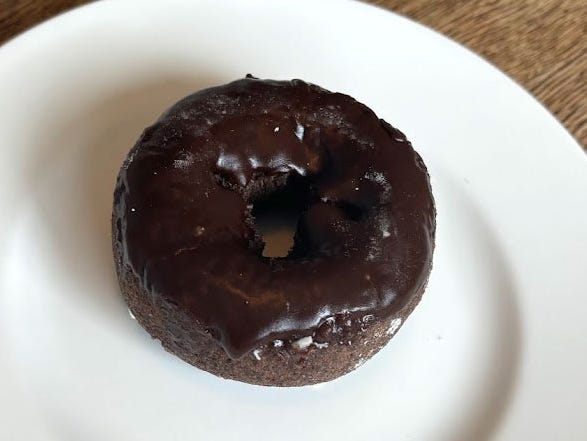 A chocolate doughnut with chocolate icing on a white plate.