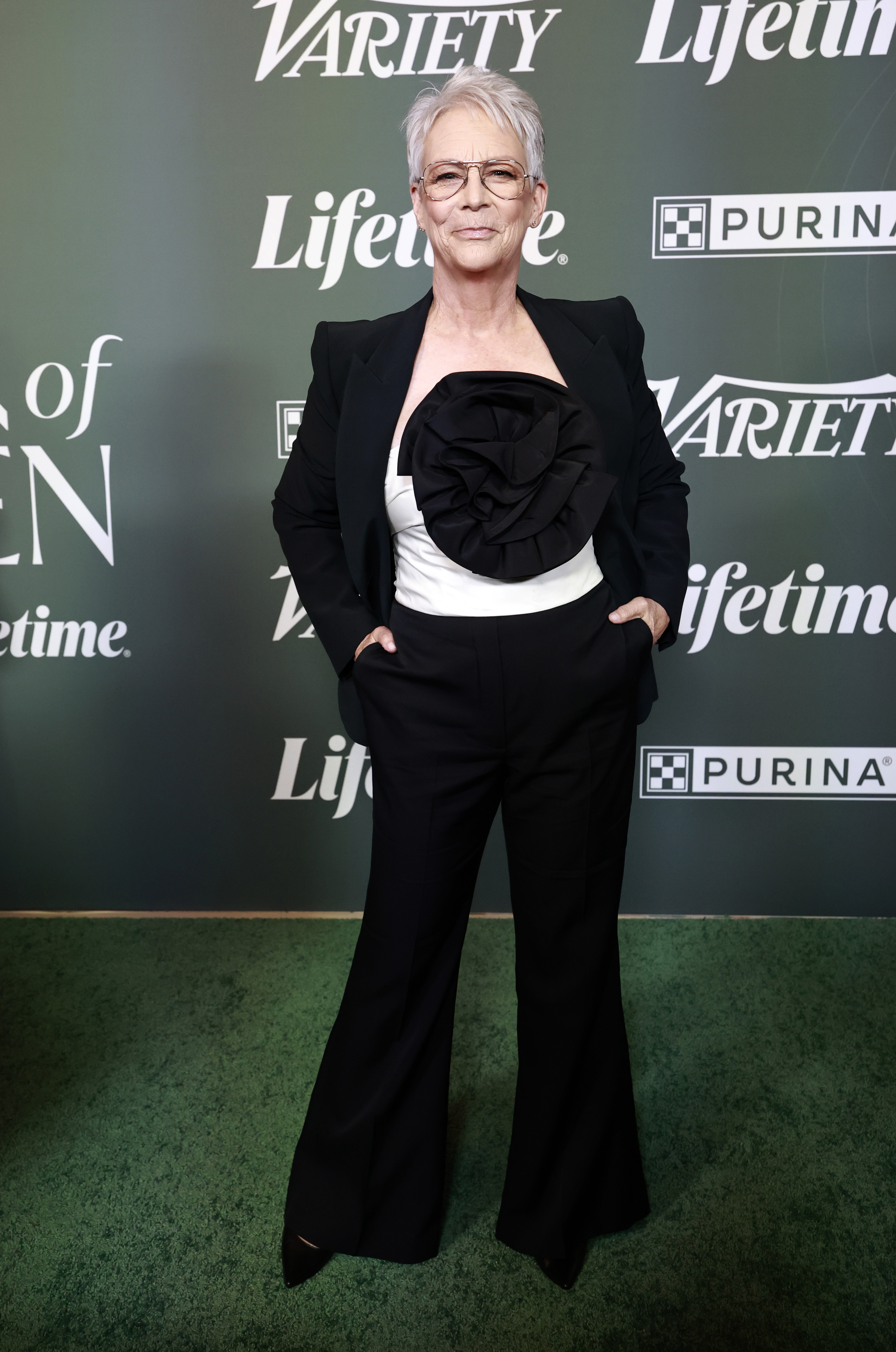 Jamie Lee Curtis in a black blazer, white strapless top with a large black floral embellishment, and black pants.