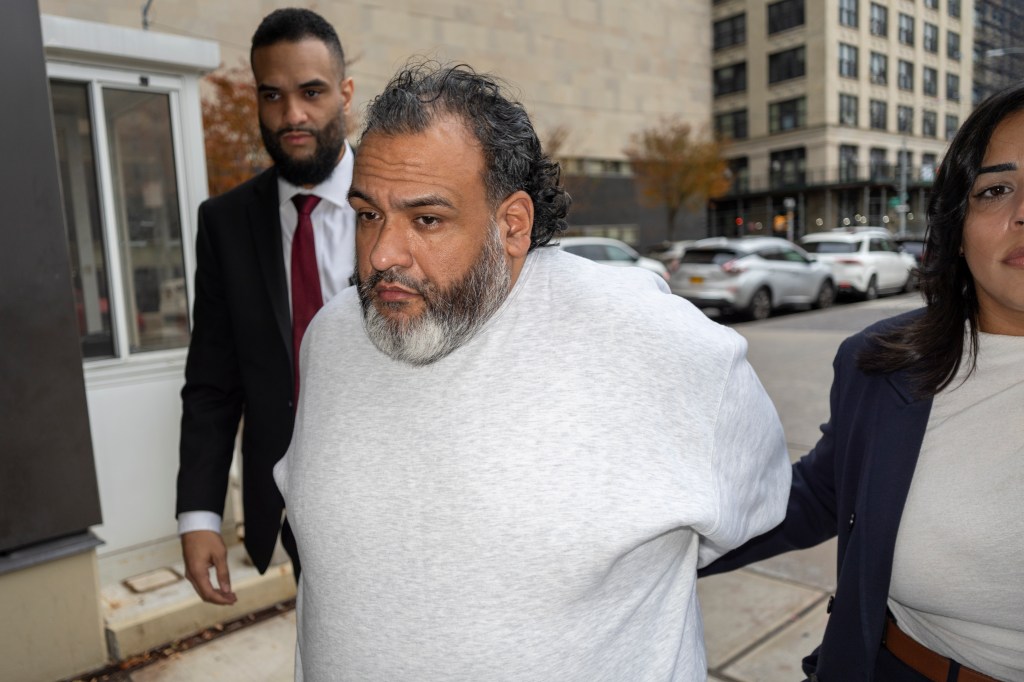 Domingo Vasquez Rodriguez, in a light grey shirt, being escorted by a man in a suit and a woman.