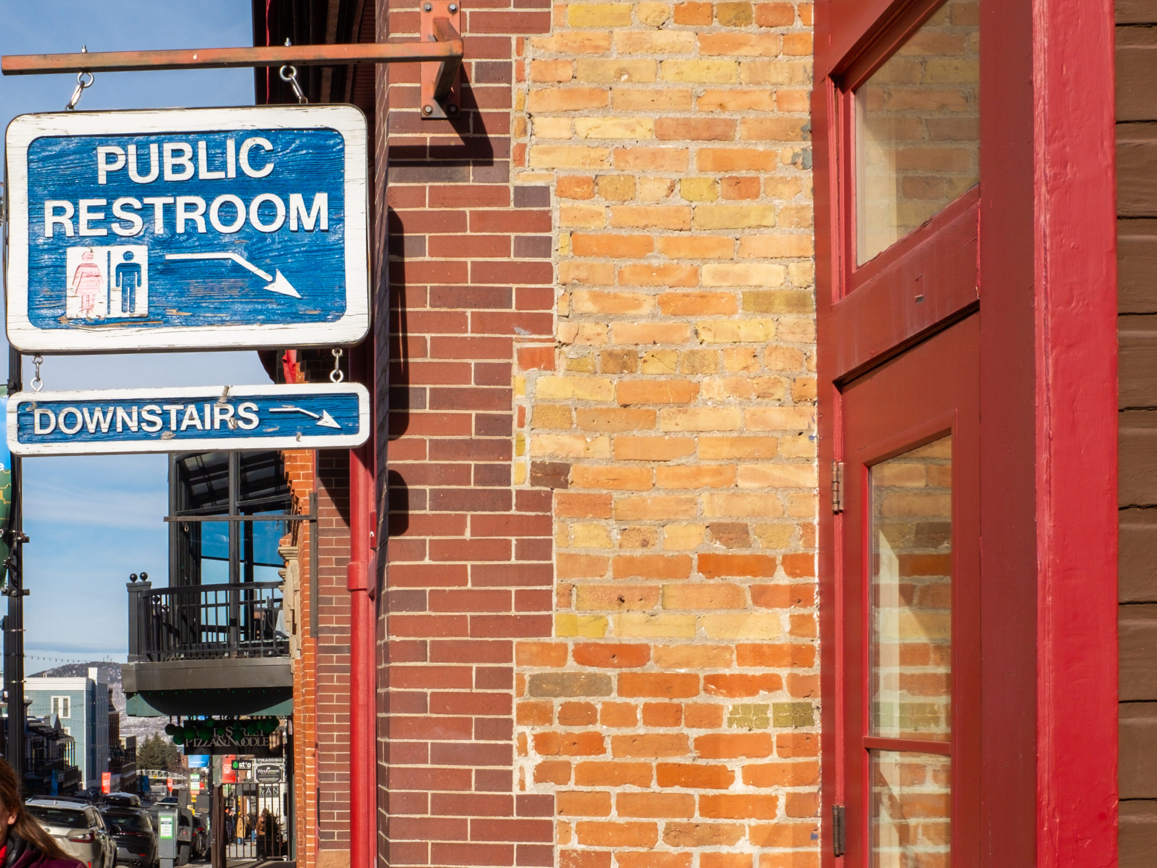 A sign for a public restroom to the left of a brick wall