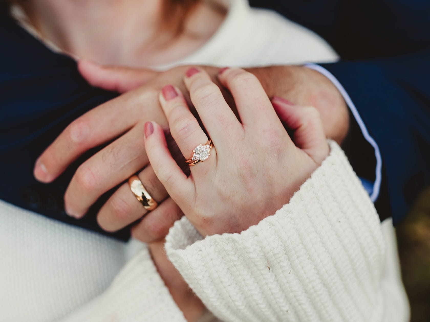 A close-up of the hands of two people embracing. Both have wedding rings on their fingers.