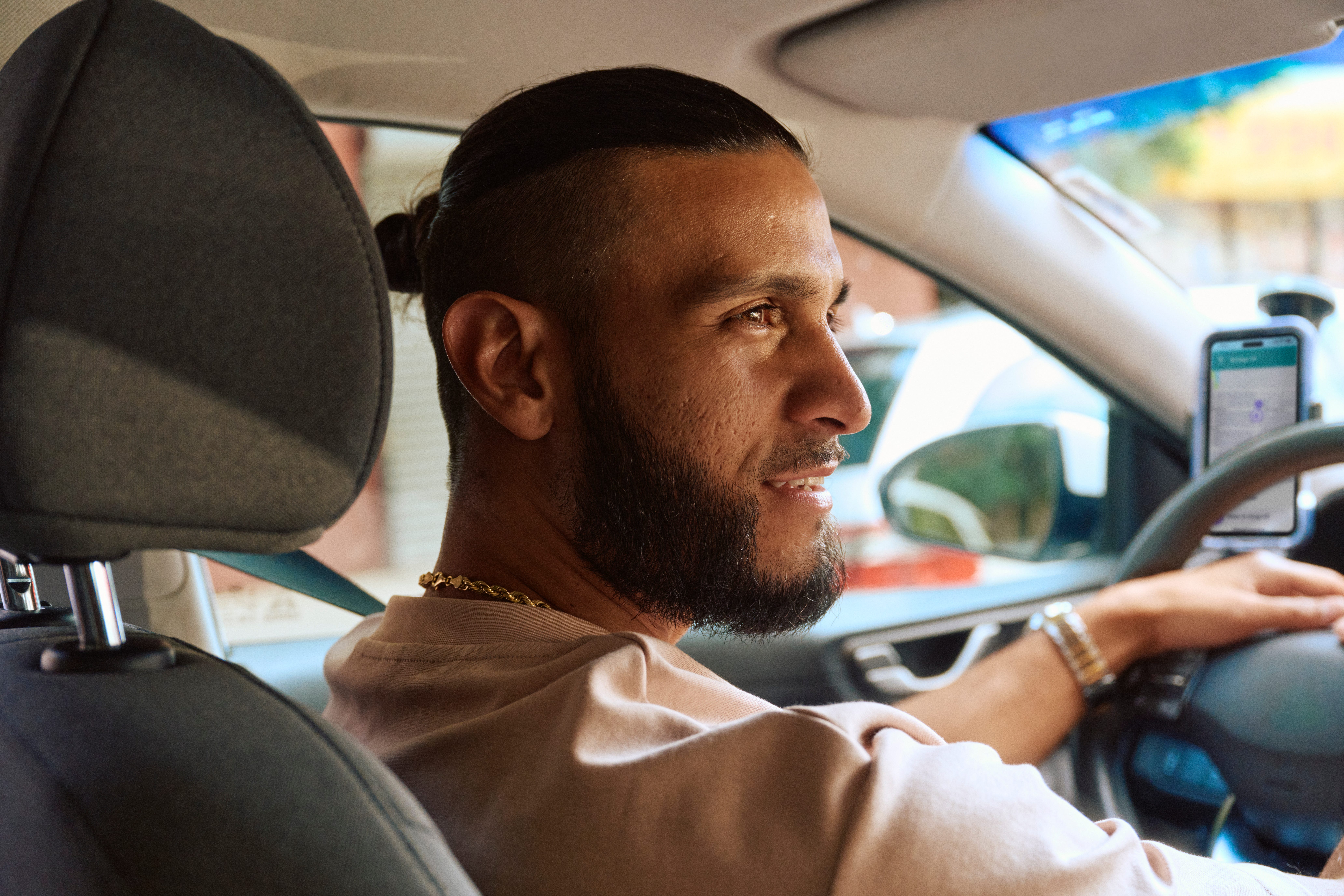 A man with his hair in a small bun looks to the right while driving a car for Lyft.