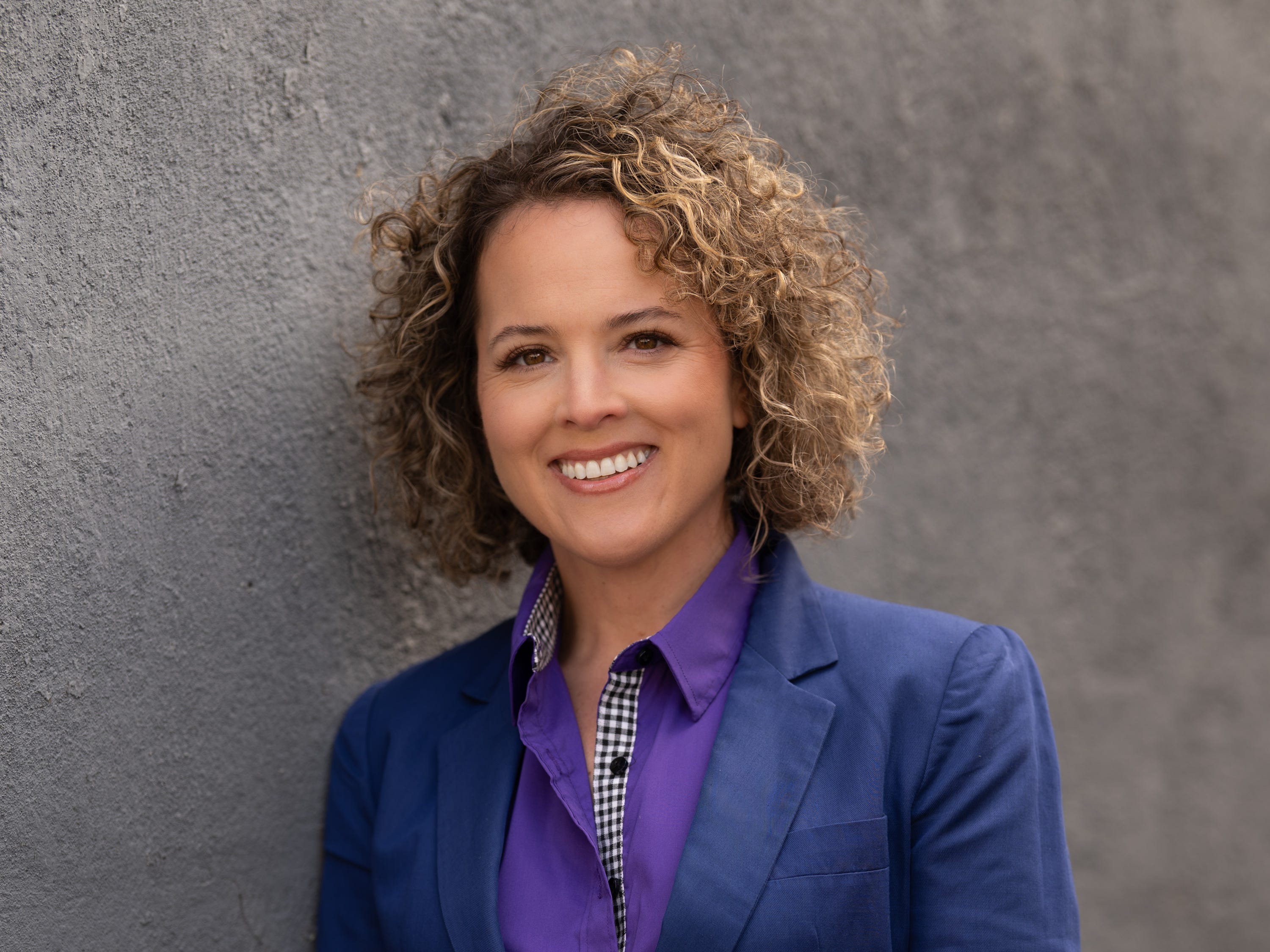 A portrait photo of dietitian Ashley Koff in a royal blue suit next to a dark gray background.