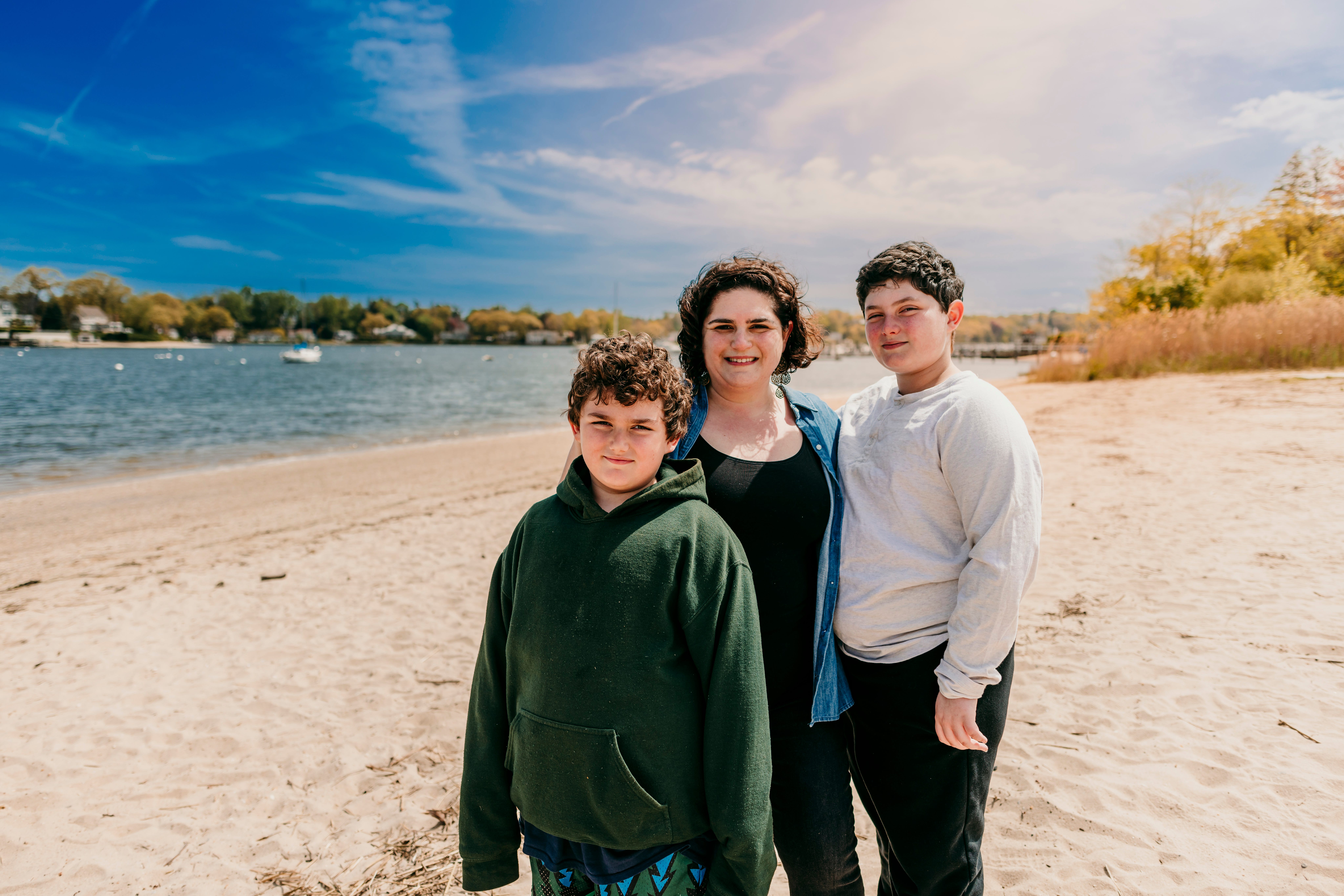 The author poses with her sons in May 2024 on a beach with small boats in the background.