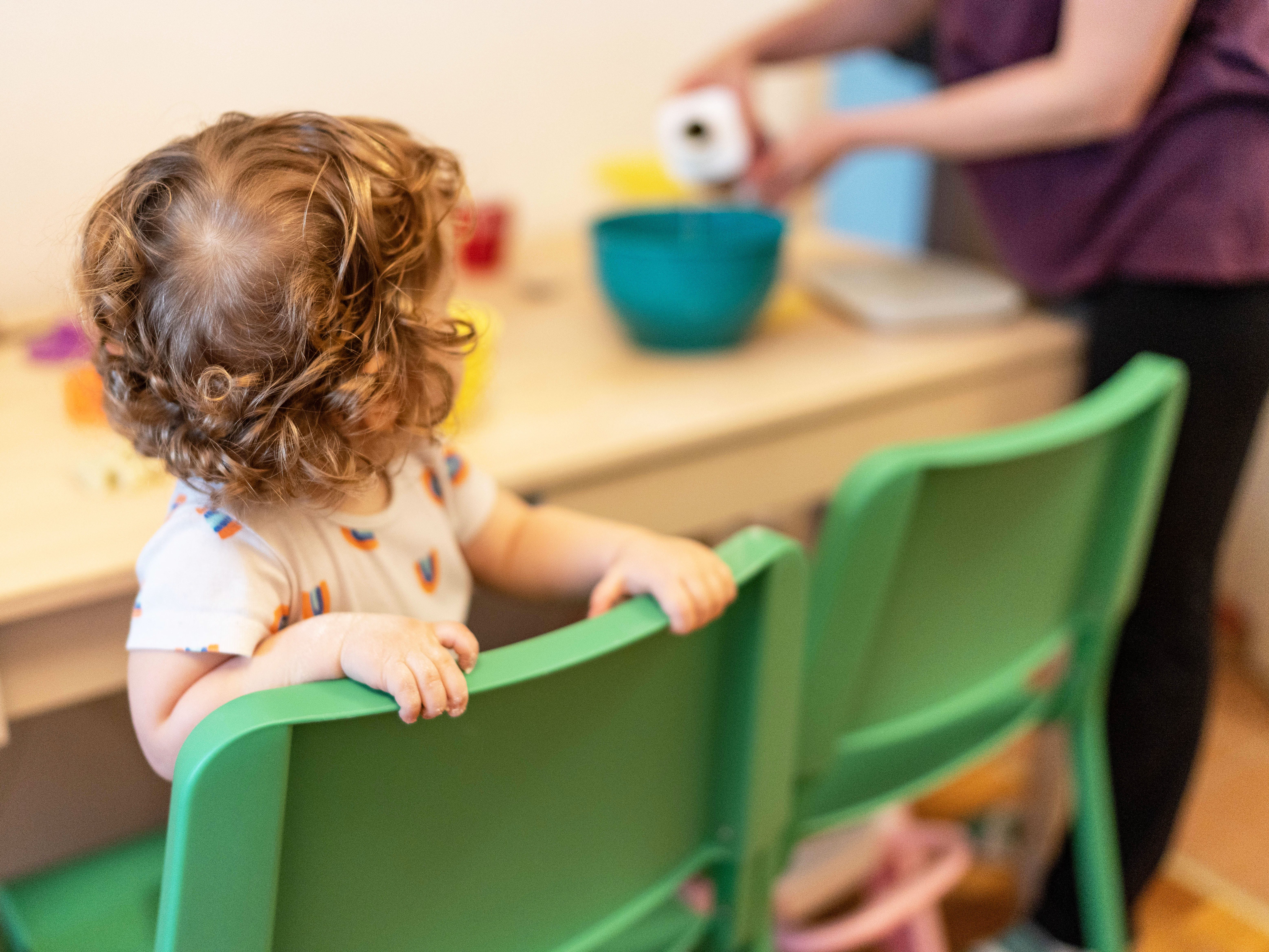 A child holding the back of a green chair