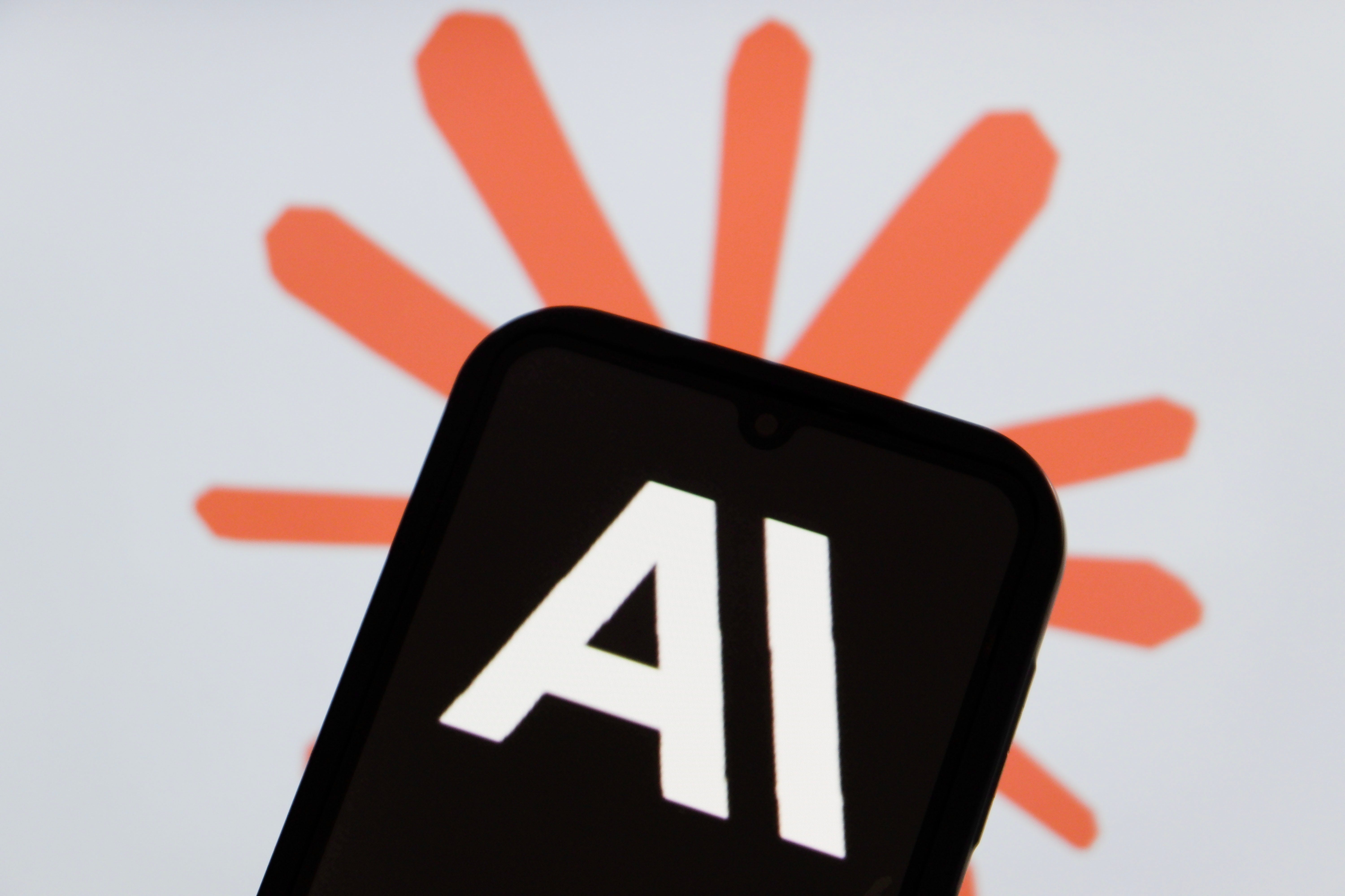 The Anthropic logo is displayed on a smartphone with Claude AI logo in the background.