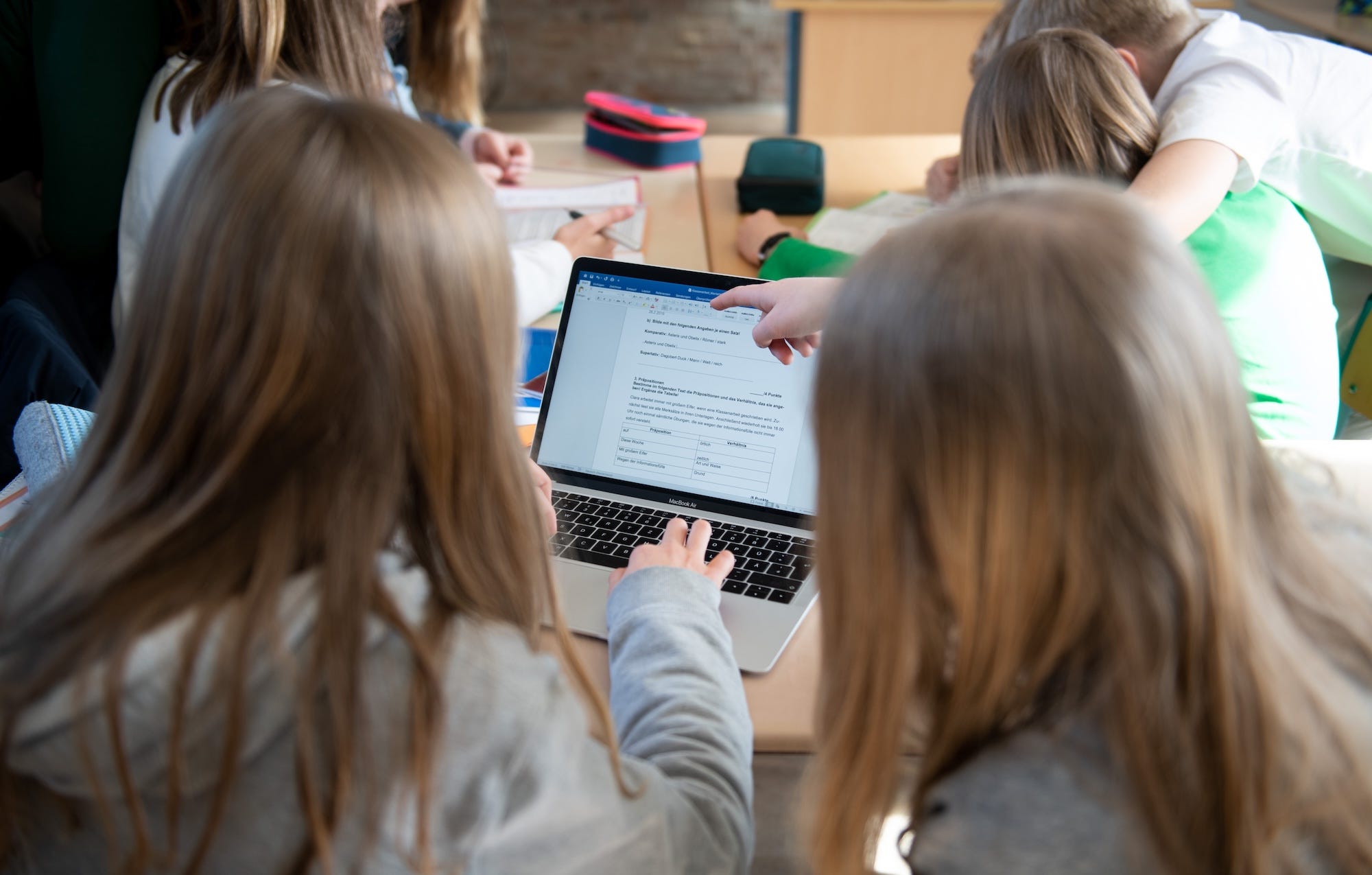 A group of schoolchildren crowd around a MacBook Air during class.