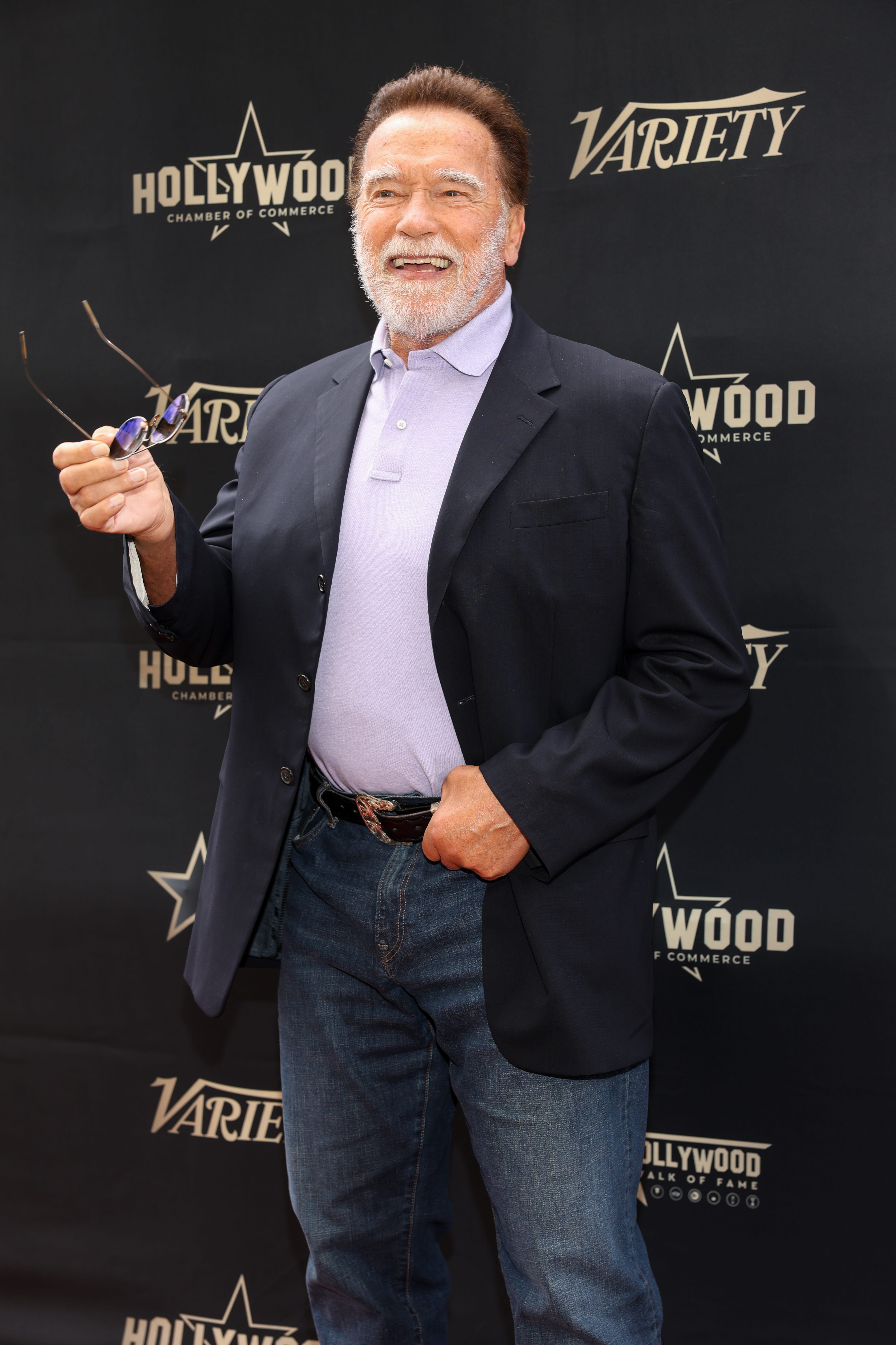 A press photo of Arnold Schwarzenegger on the red carpet at a Hollywood event in jeans and a suit jacket.
