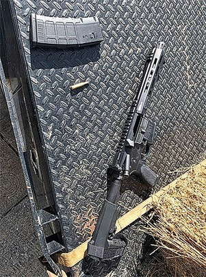An AR-style rifle, magazine, and a single bullet resting on a textured metal surface.