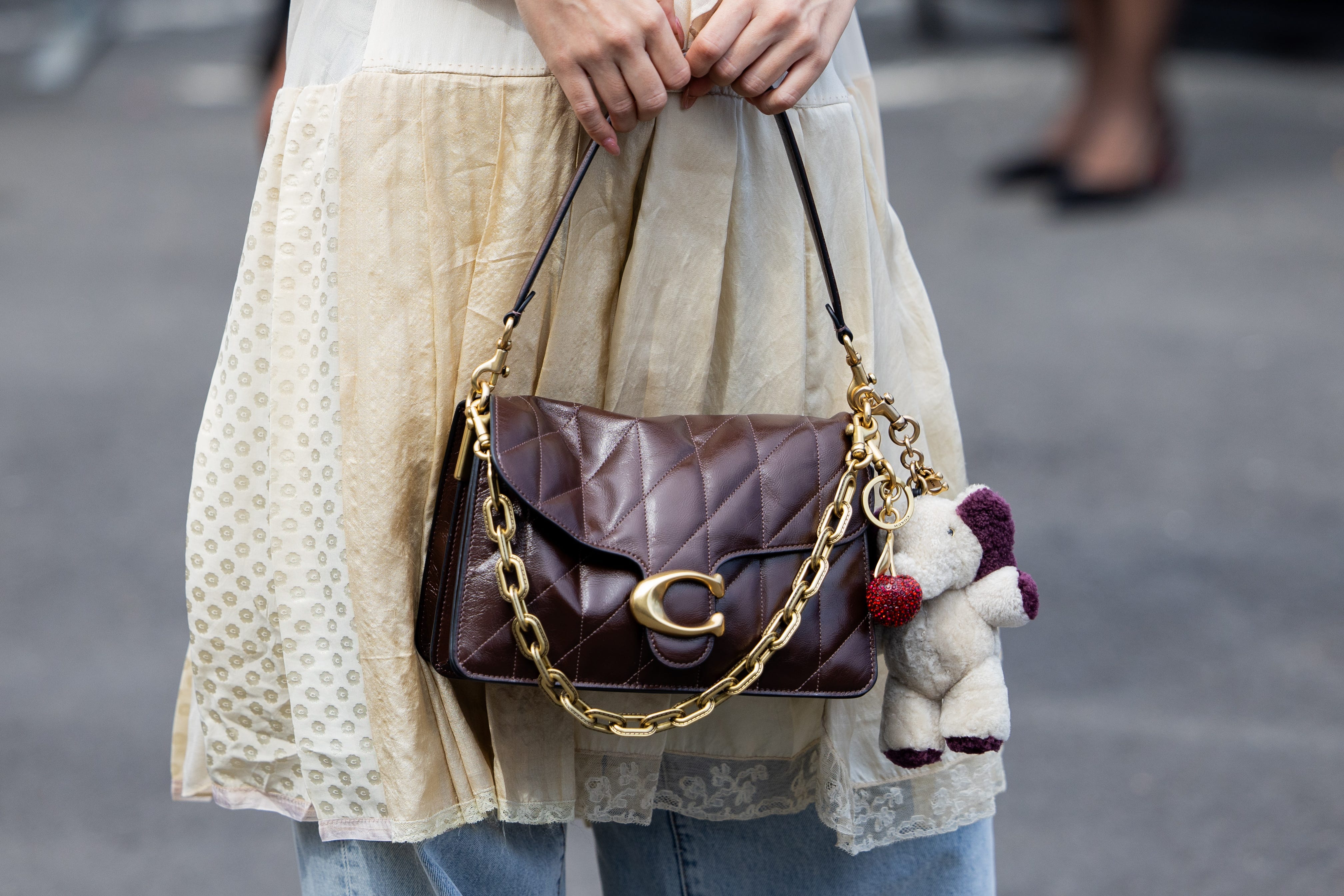 A guest wears beige pleated dress, jeans, bag outside Coach during New York Fashion Week on September 15, 2025 in New York City.